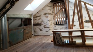 Une chambre mansardée avec un plafond en pente, un puits de lumière, une porte en bois rustique et une petite bibliothèque en bois.