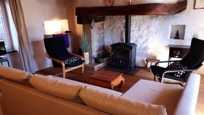 Un salon chaleureux avec un canapé, deux fauteuils, une table basse en bois, une cheminée et un mur en pierre.