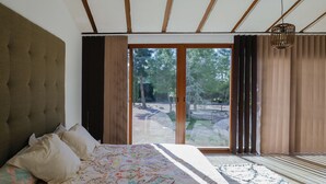 A bedroom with a large bed, a wooden headboard, and a view of the outdoors through a sliding glass door.