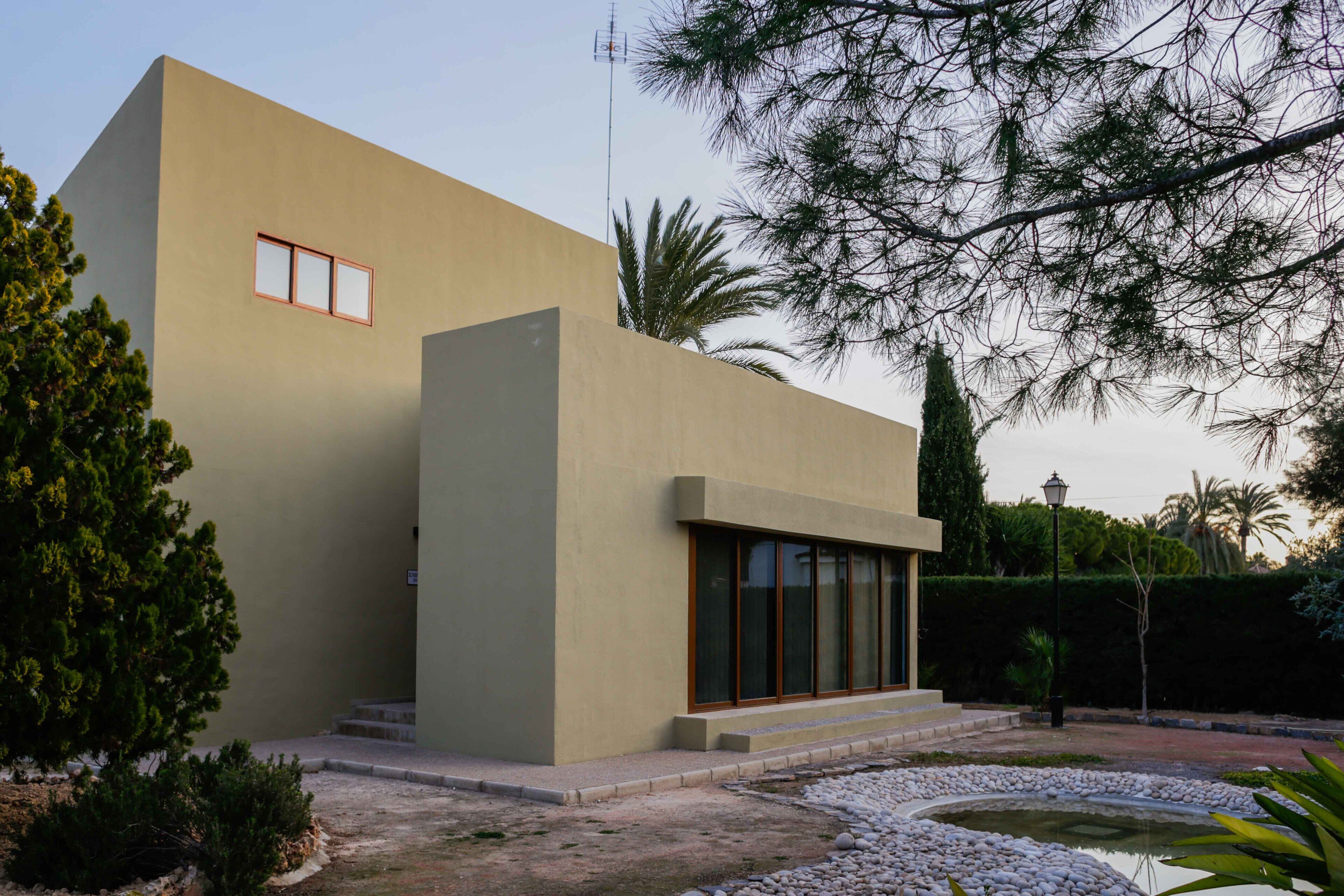 A modern building with a flat facade, large windows, and a small garden area with a water feature.
