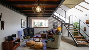 A cozy living room with a fireplace, comfortable seating, a staircase, and a large window.