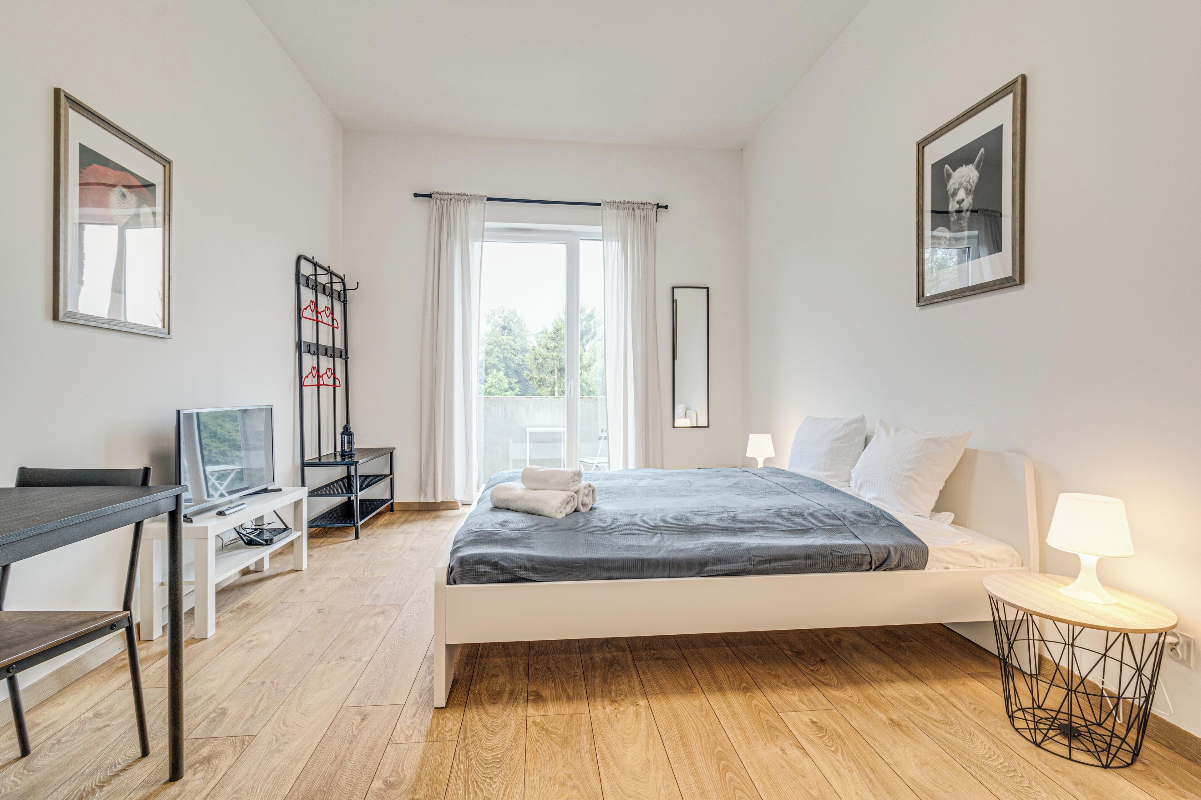 A bedroom with a bed, bedside table, desk, and a window with curtains.