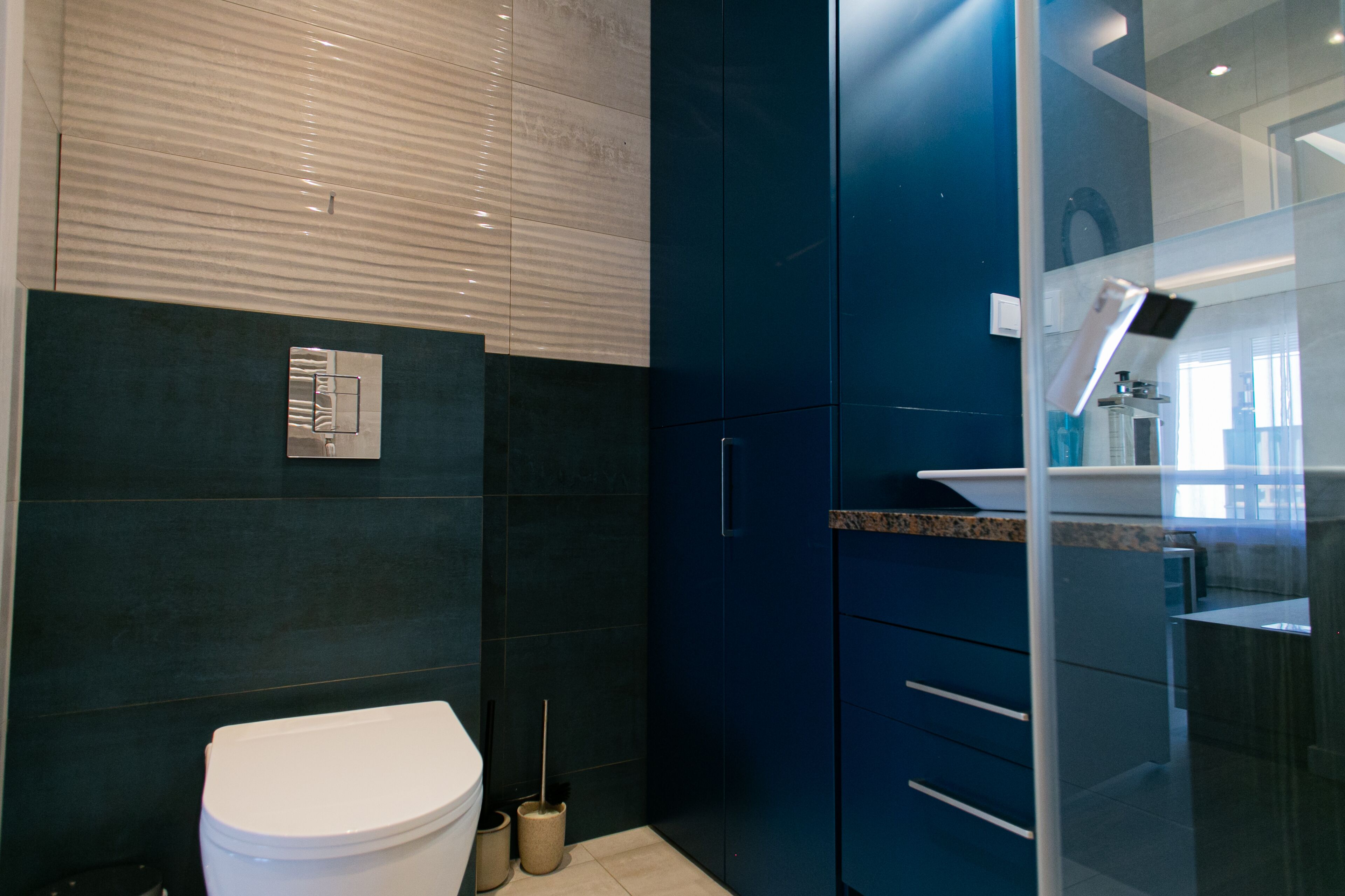 A modern bathroom with a toilet, dark blue cabinets, and a glass shower enclosure.