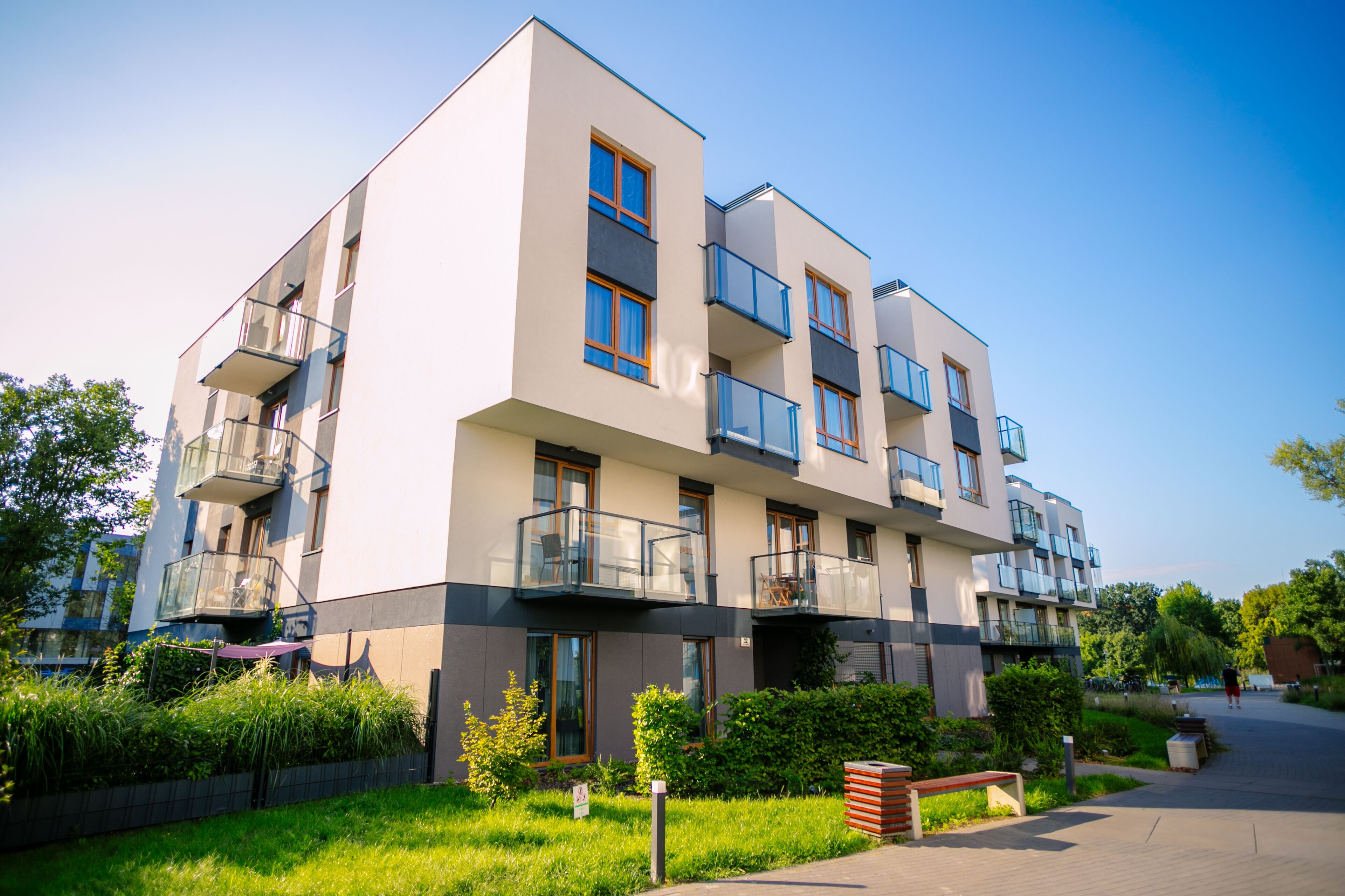 A modern multi-story residential building with balconies, a well-maintained lawn, and a clear sky.