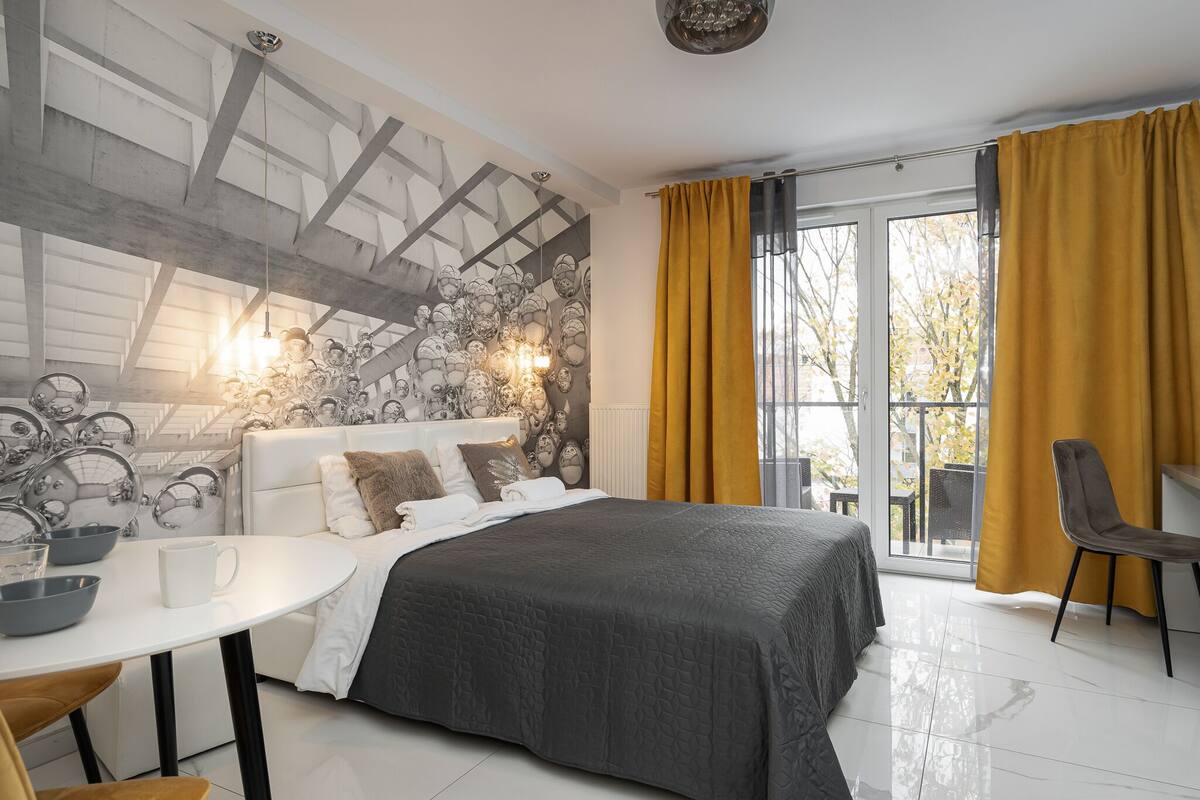 A modern bedroom with a large bed, a white round table, and a view of the outdoors through a sliding glass door.