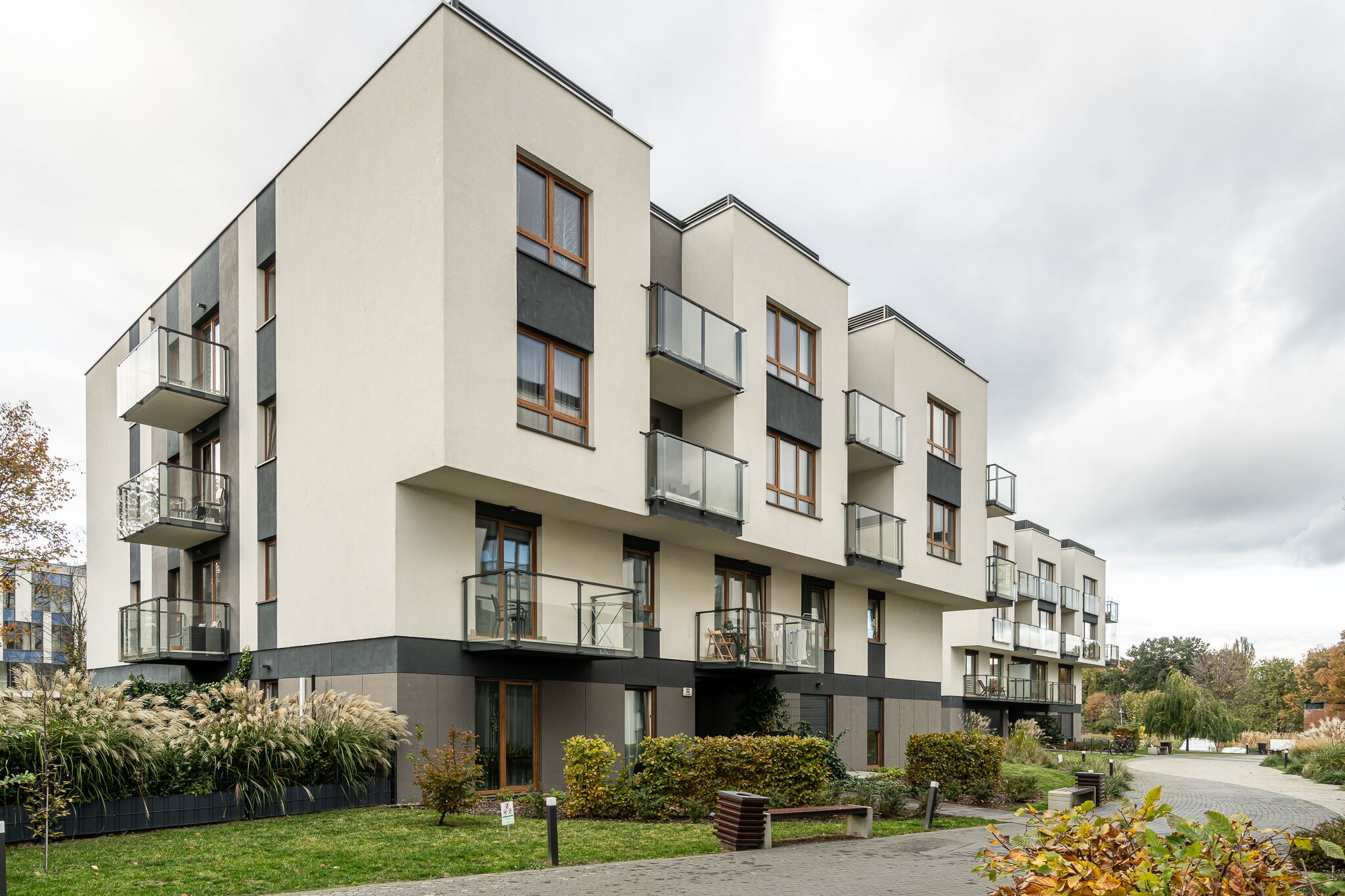 Un edificio residencial de varios pisos con balcones, un patio empedrado y vegetación circundante.