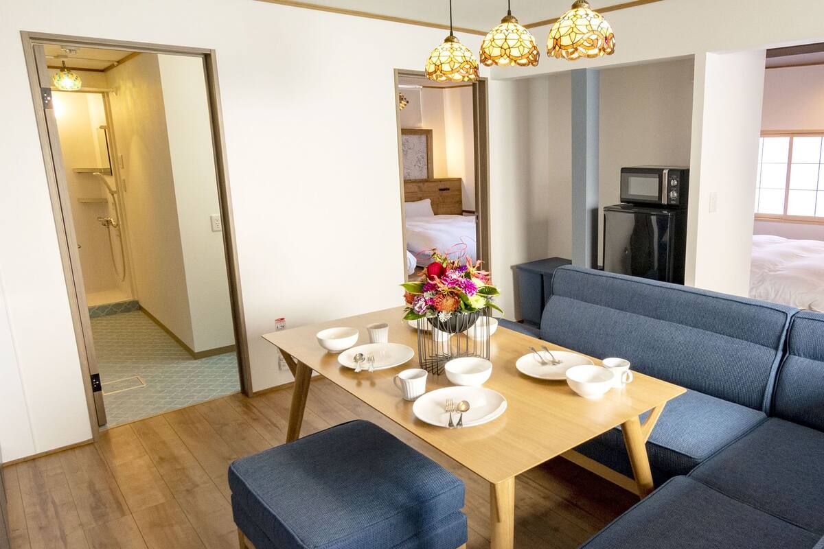 A modern hotel room with a dining area, a sofa, a microwave, and a bed.