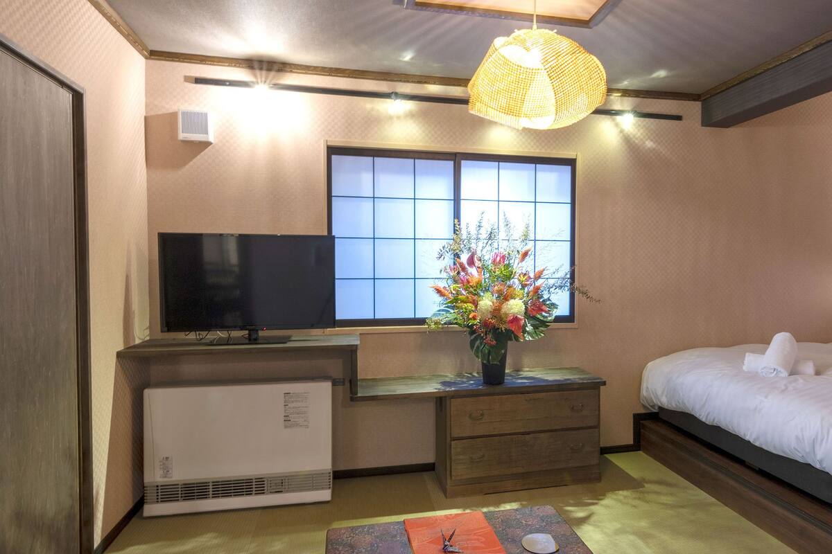 A hotel room with a bed, a desk with a computer, a window with a view, and a decorative plant.