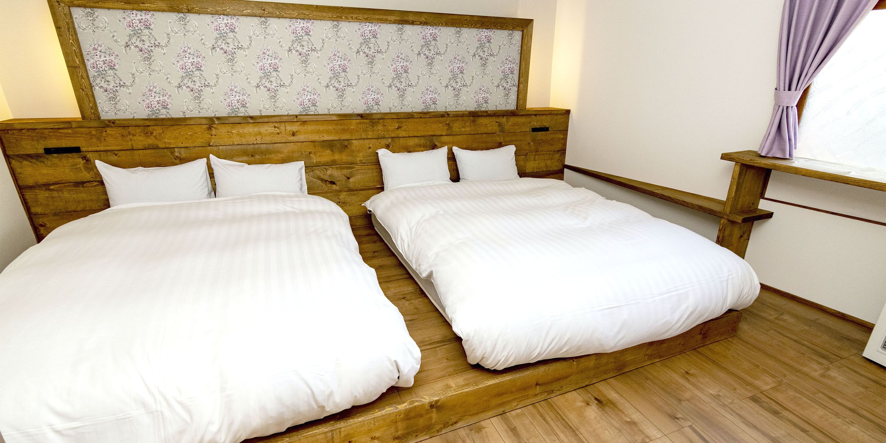 A double bed with a wooden headboard and a floral-patterned wall above.