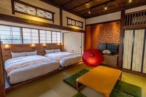 A traditional Japanese-style room with two beds, a wooden table, and a red fan. - Ebisumachi Takadaya (Hakodate)