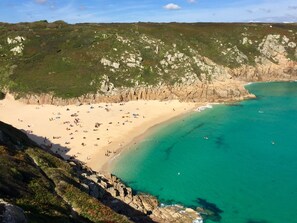 A coastal landscape with a sandy beach, clear turquoise waters, and rocky cliffs.