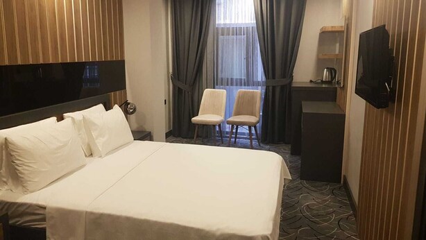 A hotel room with a large bed, two chairs, a desk, and a TV. - Pozcu Otel (Mersin)