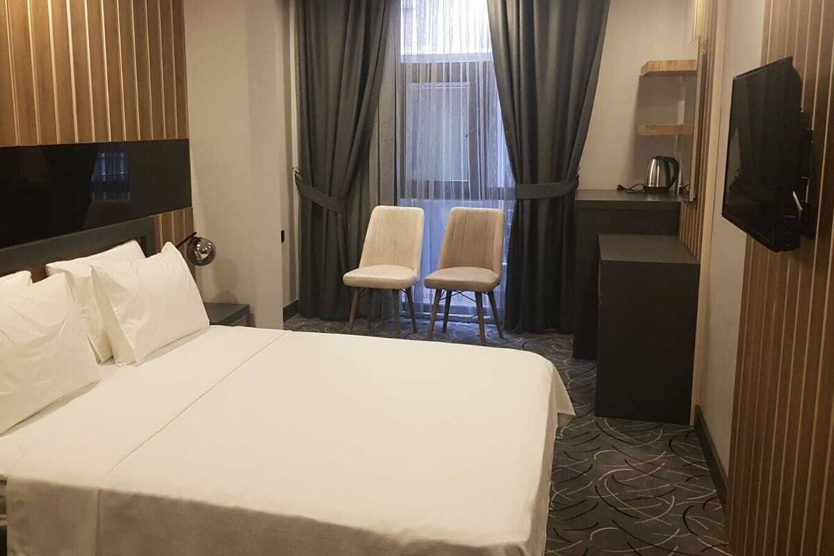A hotel room with a large bed, two chairs, a desk, and a TV.