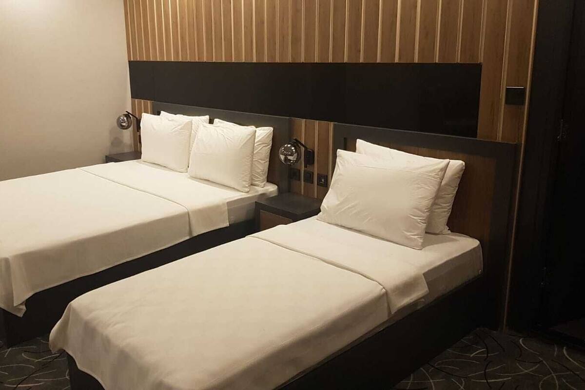 Two single beds with white linens in a room with wooden paneling and a dark headboard.