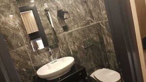 A bathroom with a marble wall, a sink, a toilet, and a mirror. - Pozcu Otel (Mersin)