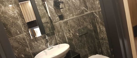 A bathroom with a marble wall, a sink, a toilet, and a mirror.