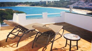 Une terrasse avec deux fauteuils et une petite table, d’où l’on a vue sur une plage et une ville côtière.