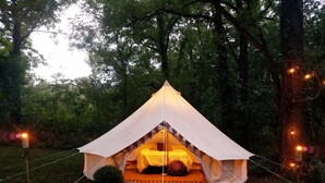 A tent with a bed inside, surrounded by trees and string lights. - Large Bell Tent on the Kings River! (Eureka Springs)