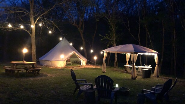 A tented camping area with a picnic table and chairs, string lights, and a canopy. - Large Bell Tent on the Kings River! (Eureka Springs)