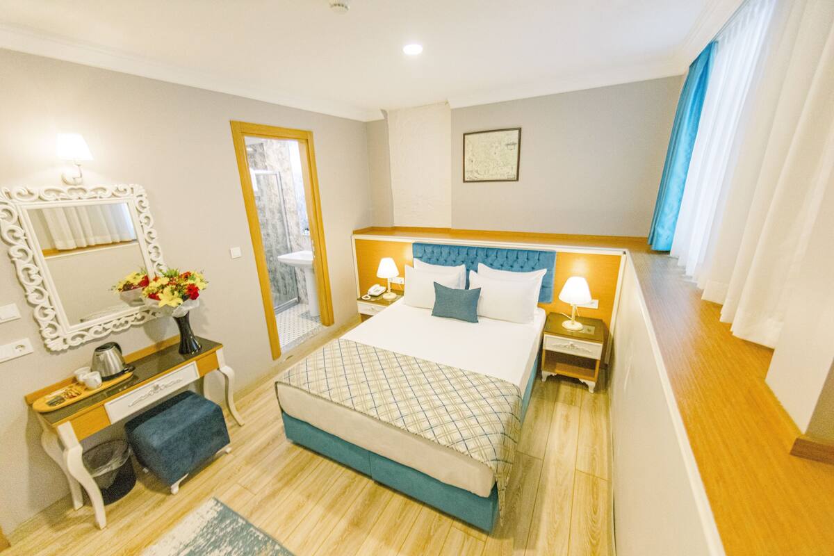 Une chambre d’hôtel avec un lit, des tables de chevet, un miroir, un bureau et une fenêtre avec des rideaux.