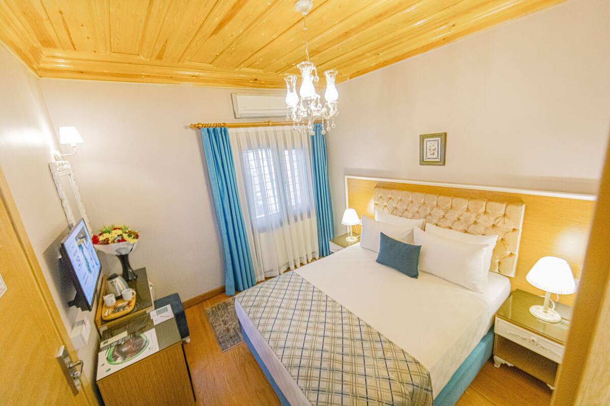 Une chambre d’hôtel avec un lit, des tables de chevet, une télévision et un lustre.