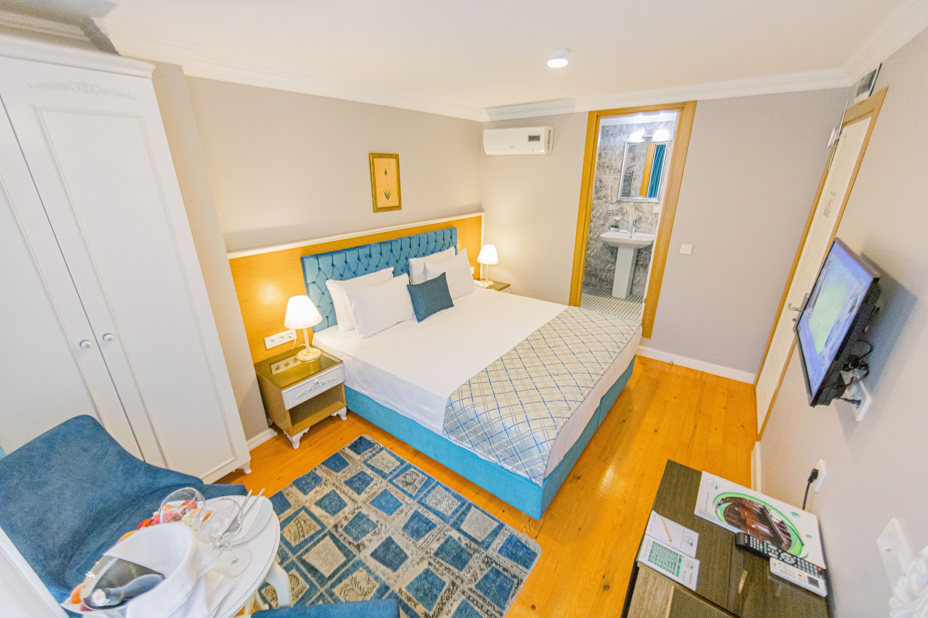 A hotel room with a bed, bedside table, lamp, TV, and a blue chair.