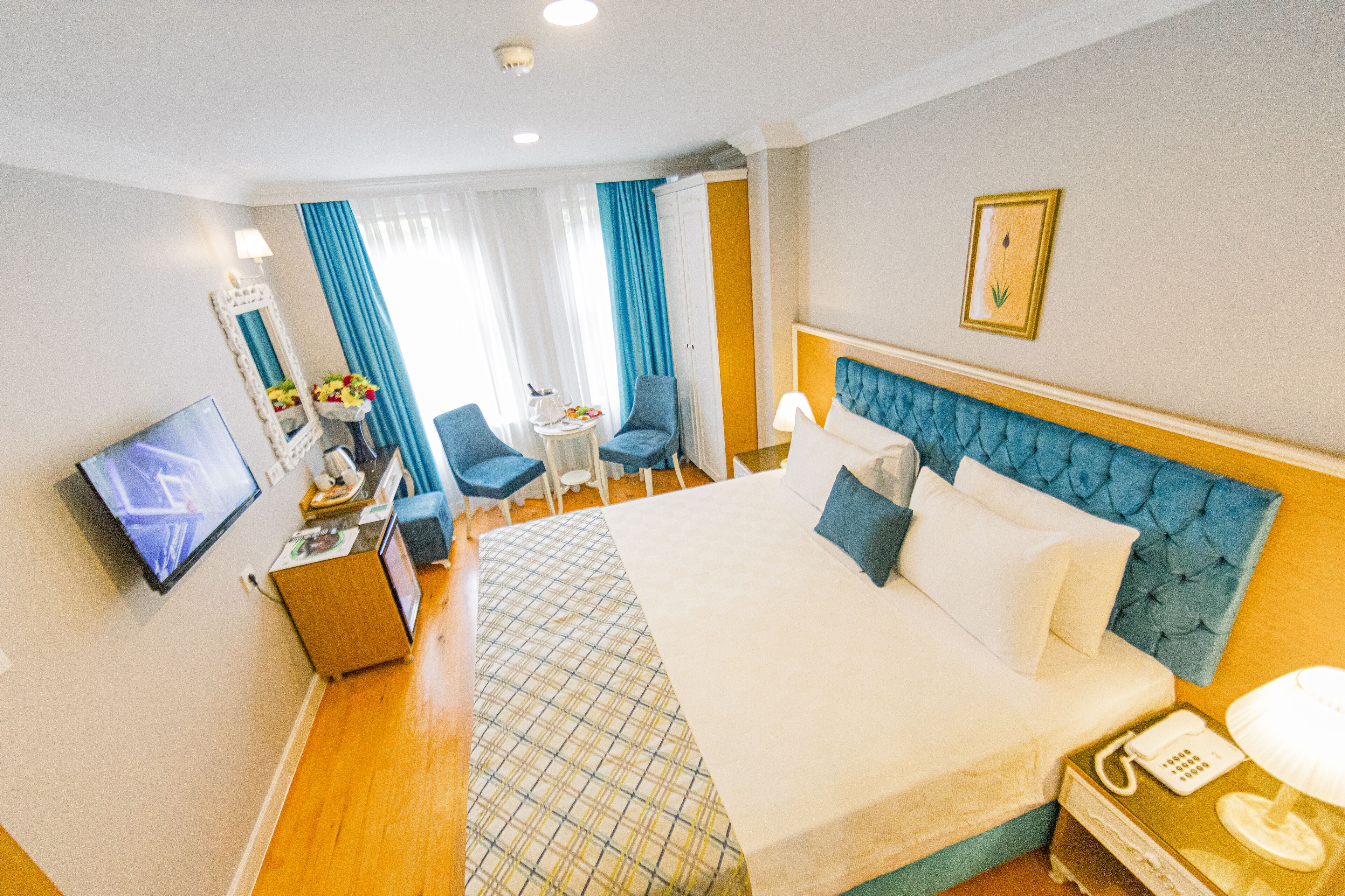Une chambre d’hôtel avec un grand lit, une télévision, un bureau avec une chaise et une fenêtre avec des rideaux.