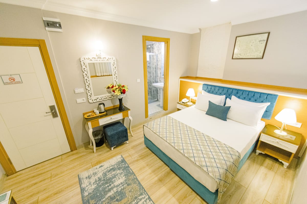 Une chambre d’hôtel avec un lit, des tables de chevet, une commode, un miroir et une porte de salle de bain.