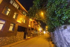 A narrow street lined with brick buildings, some with illuminated signs, and a stone wall on one side. - Acacia Mansion Hotel (Istanbul)