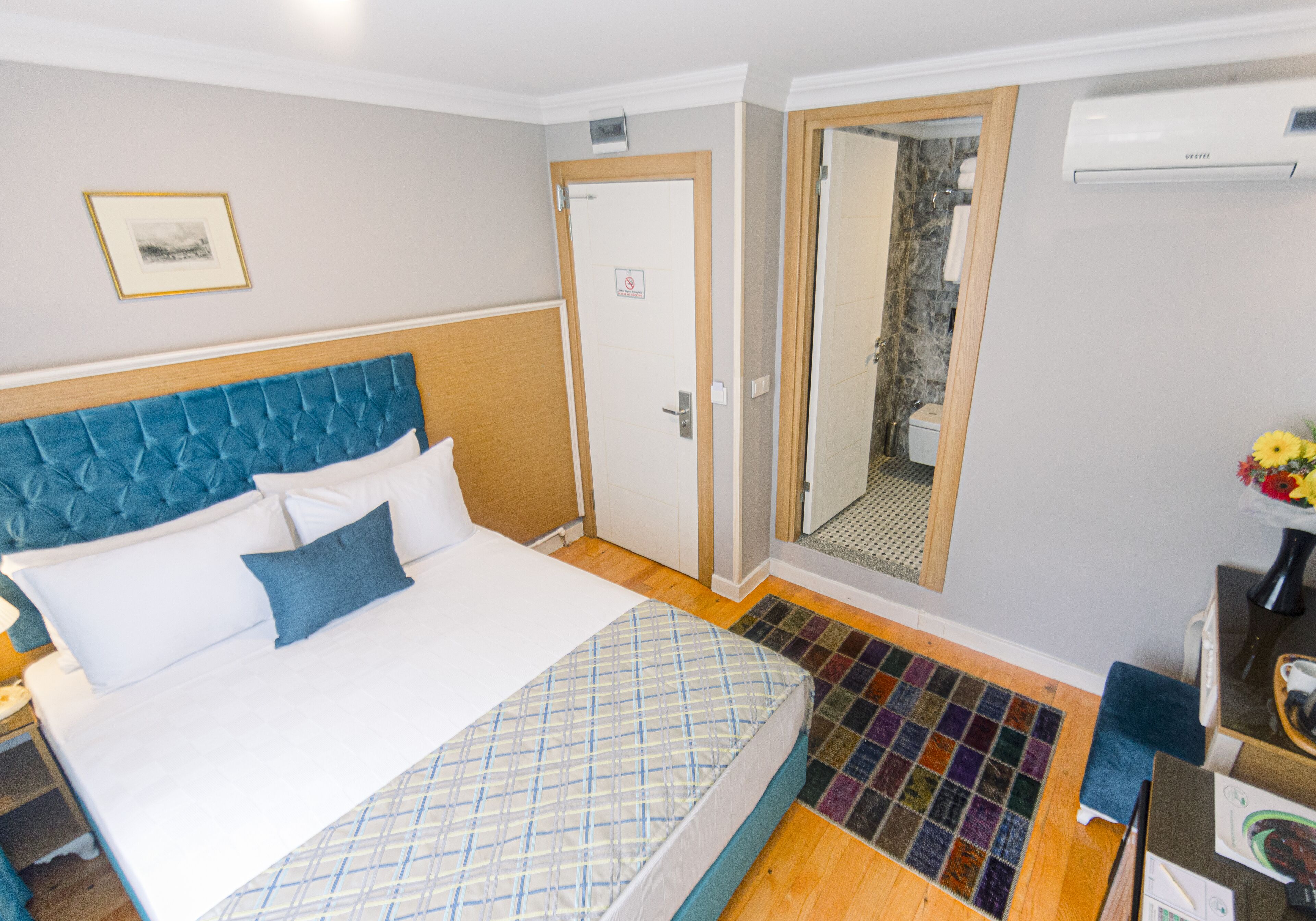 Hotelkamer met een groot bed, een badkamer met douche en een tafeltje met een bloevas.