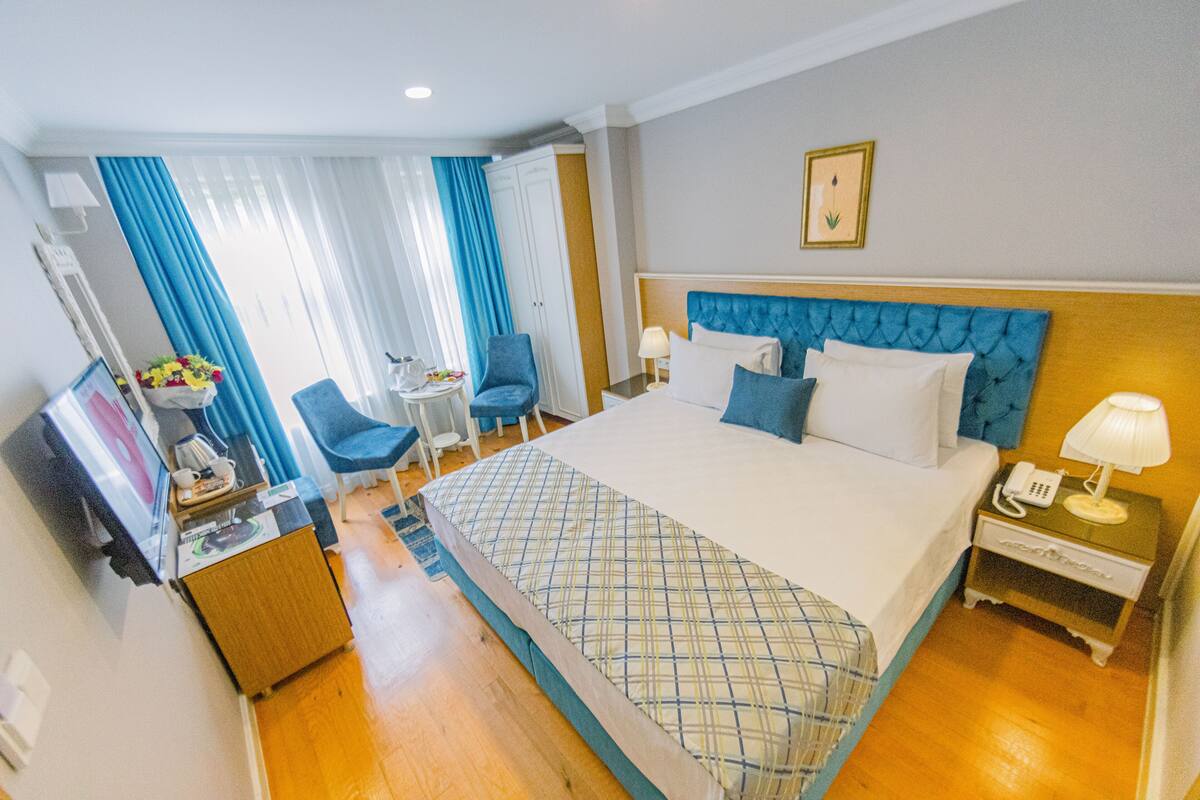 Une chambre d’hôtel avec un grand lit, un bureau avec une chaise, une petite table et une chaise bleue.