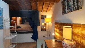 Quarto pequeno e acolhedor com uma cama de solteiro, uma mesa de cabeceira, uma luminária e uma prateleira na parede.