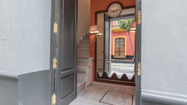 A hallway with a dark door, a staircase, and a view of a building with a clock and a window. - Tourist apartment, located in the center of Seville (SEVILLA)