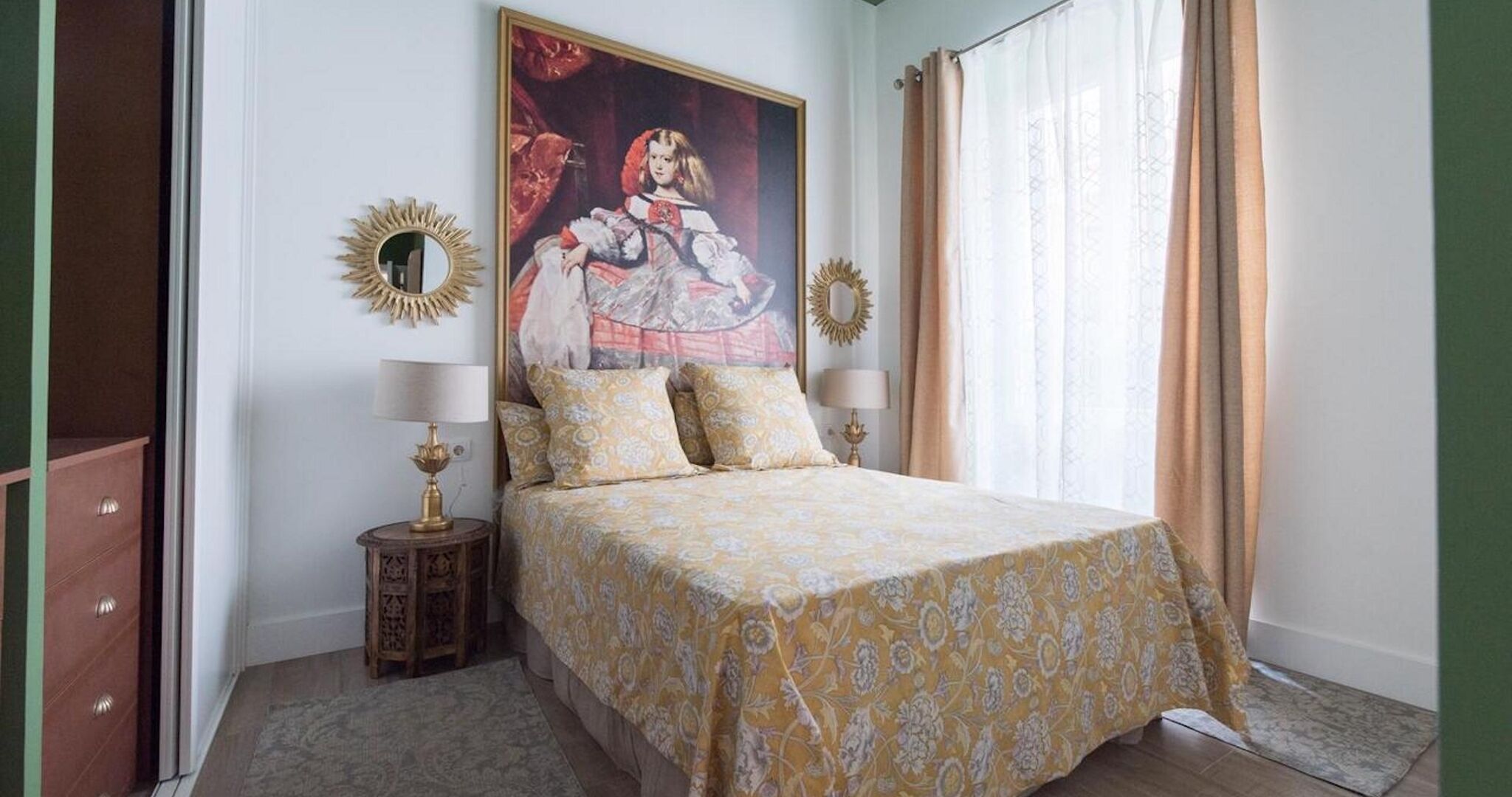 A bedroom with a bed, two bedside tables, a mirror, and a painting on the wall.