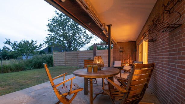 An outdoor patio with a round wooden table and four wooden chairs, surrounded by a brick wall and a wooden fence. - Spacious vacation apartment with garden, surrounded by greenery. (Westerdeichstrich)