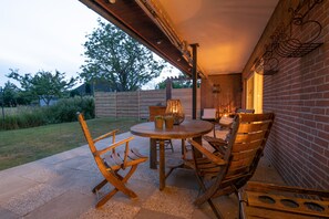 An outdoor patio with a round wooden table and four wooden chairs, surrounded by a brick wall and a wooden fence.