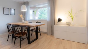 A modern dining area with a wooden table and chairs, a pendant light, and a view of greenery outside. - Spacious vacation apartment with garden, surrounded by greenery. (Westerdeichstrich)