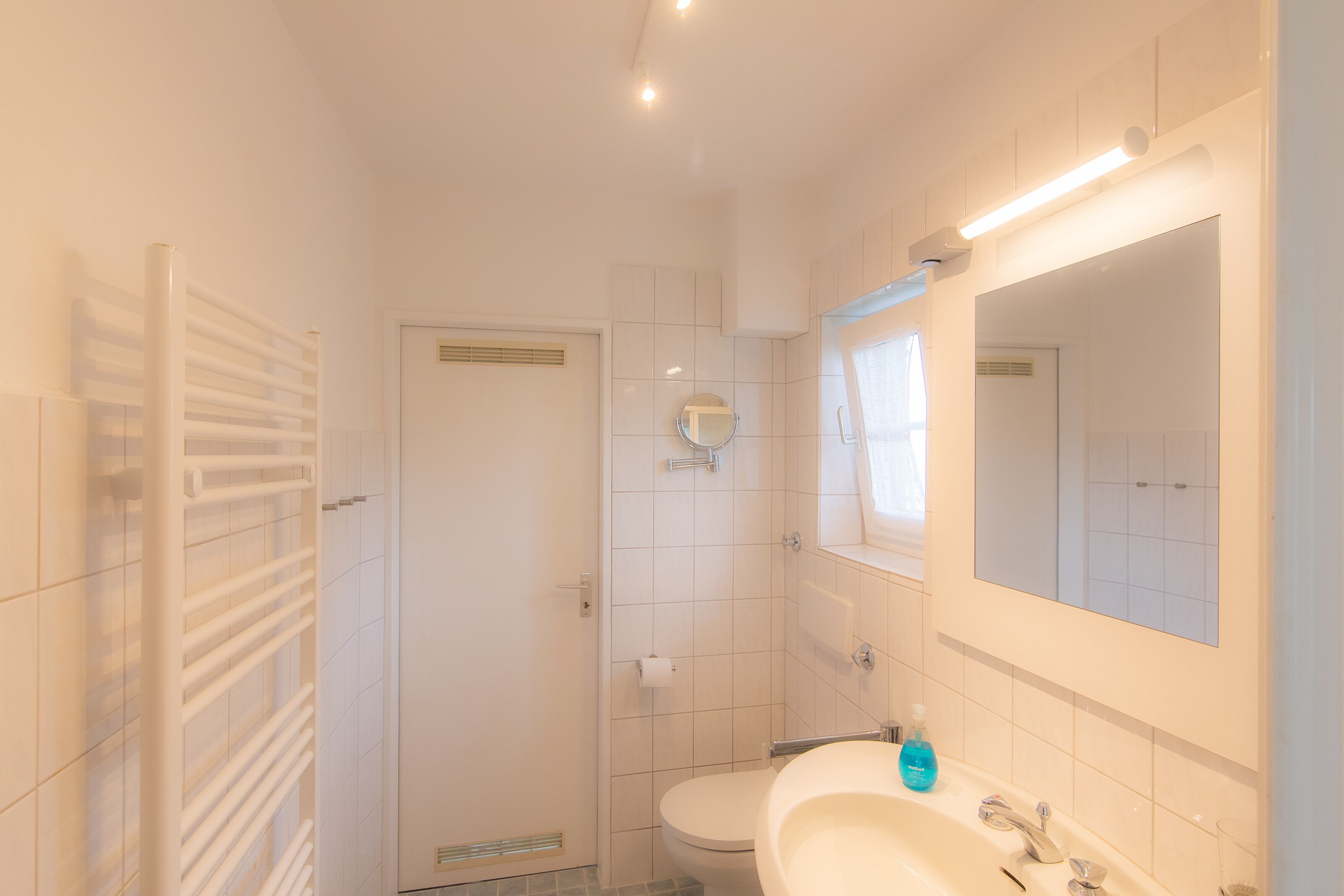 A bathroom with a toilet, sink, mirror, and towel rack.