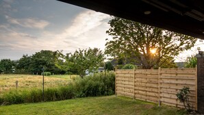 A backyard with a wooden fence, a grassy lawn, and a tree with sunlight filtering through the leaves. - Spacious vacation apartment with garden, surrounded by greenery. (Westerdeichstrich)