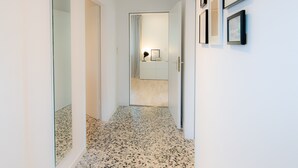 A hallway with a speckled floor, a mirror on the left, and framed pictures on the right wall. - Spacious vacation apartment with garden, surrounded by greenery. (Westerdeichstrich)