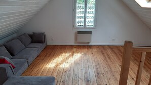 A room with a sloped ceiling, a grey sofa, a wooden floor, and a window with a view of greenery.