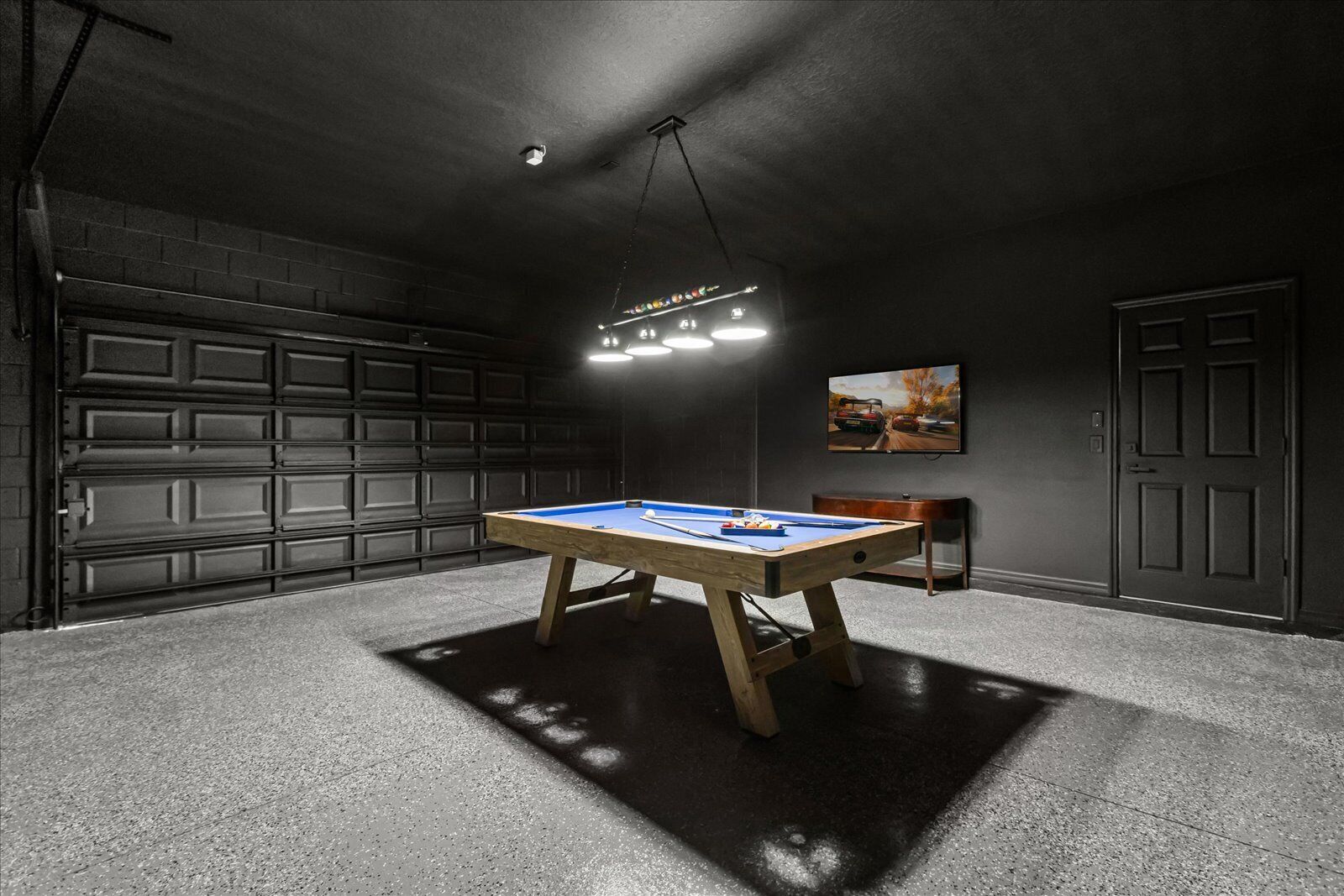 Una mesa de billar en una habitación con poca luz, con una puerta de garaje al fondo.