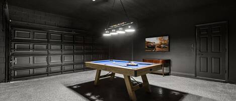 Una mesa de billar en una habitación con poca luz, con una puerta de garaje al fondo.