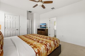 Une chambre à coucher comprenant un lit, un ventilateur de plafond, une commode et un téléviseur.
