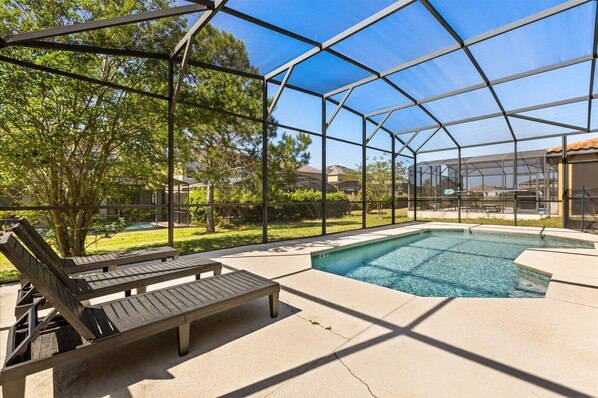 A covered outdoor swimming pool with a wooden deck and benches, surrounded by trees and houses.