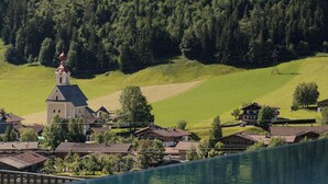 A serene lakeside view with a church, houses, and a forested hill.