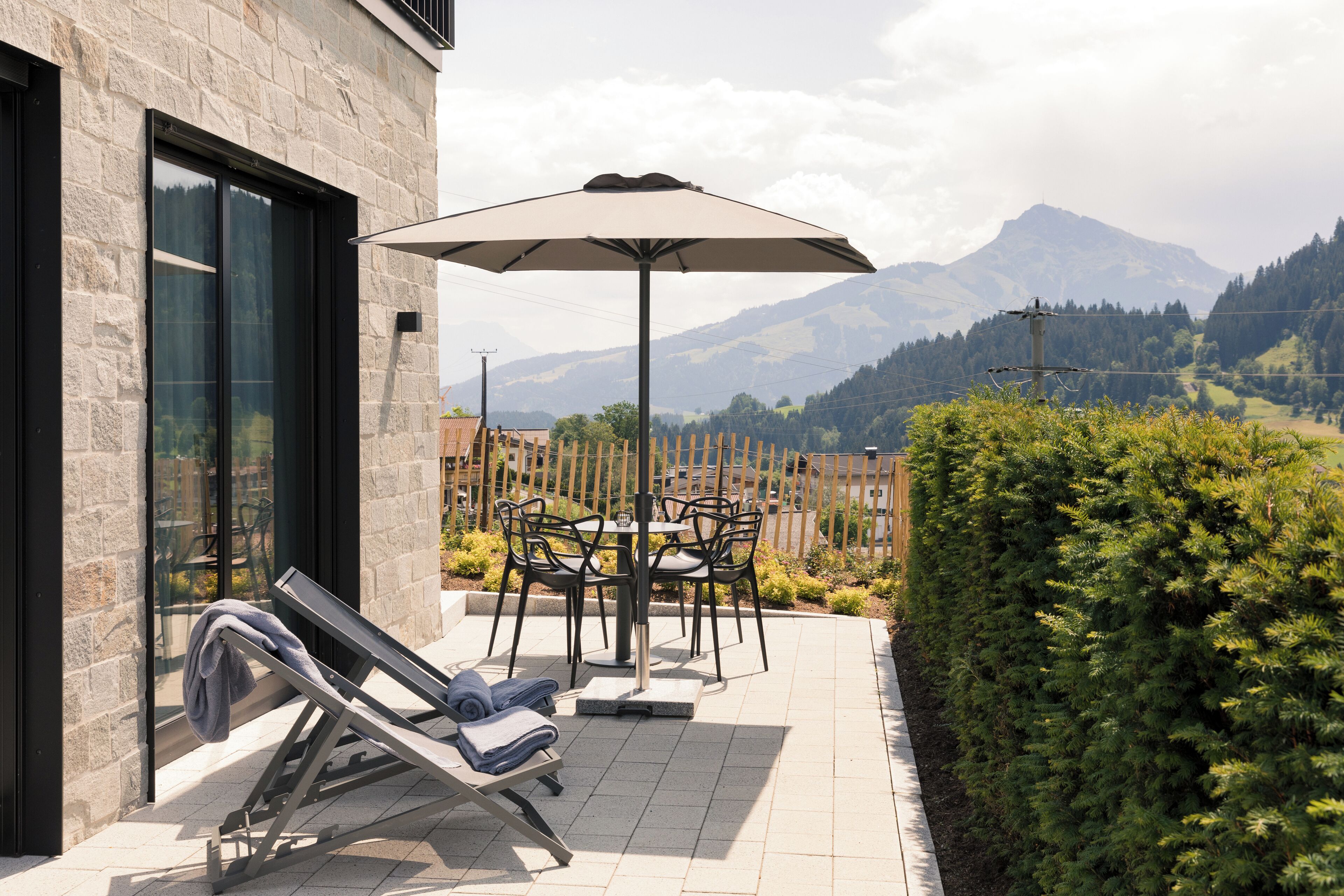 Eine Terrasse mit Tisch, Stühlen und einer Liege, sowie einem großen Sonnenschirm.
