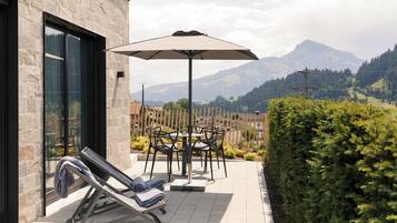 Eine Terrasse mit Tisch, Stühlen und einer Liege, sowie einem großen Sonnenschirm.