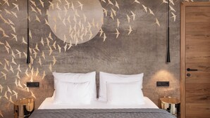 A bedroom with a large bed, two bedside tables, a wooden wardrobe, and a wall with a bird mural.