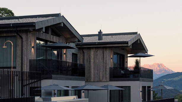 A modern multi-story building with a stone facade, a prominent 'AAA' logo, outdoor seating, and a mountain view.